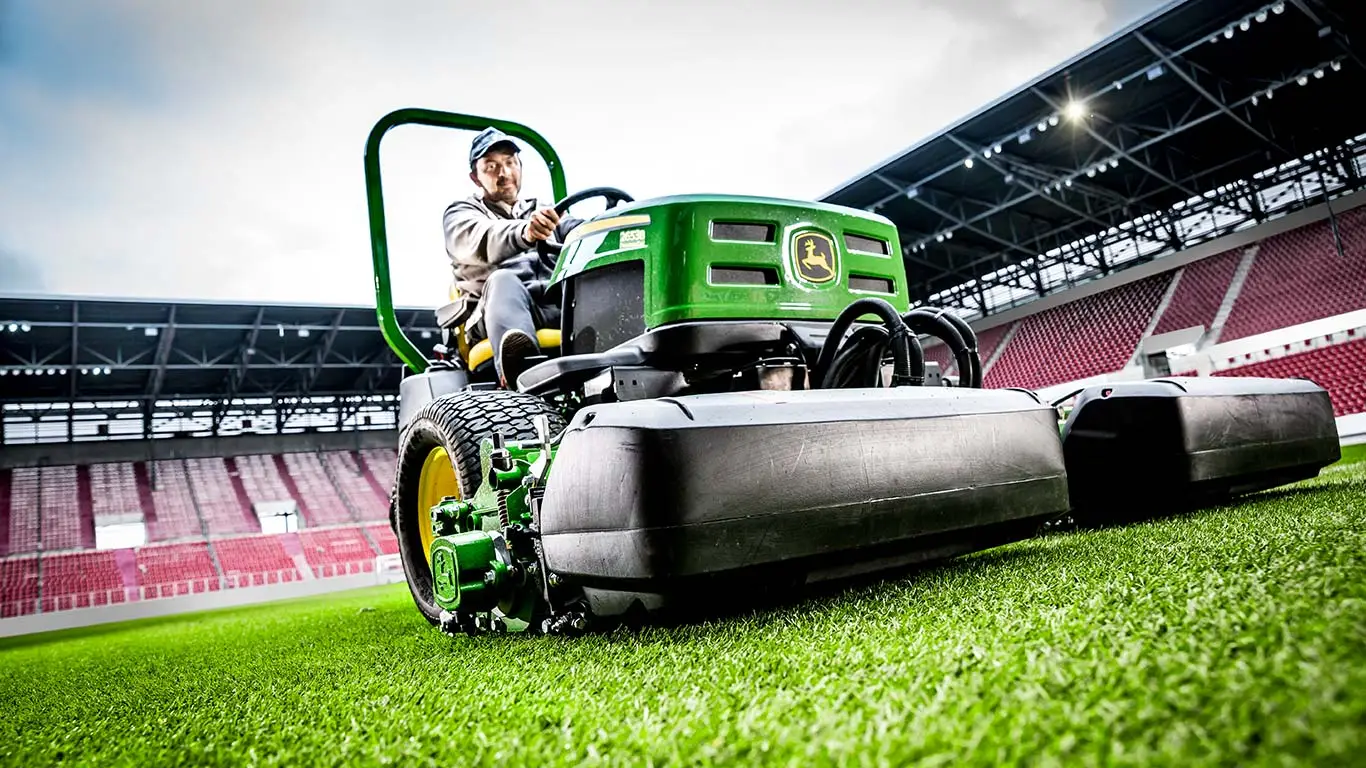 Mann auf John Deere Maschine bei der Rasenpflege im Stadion