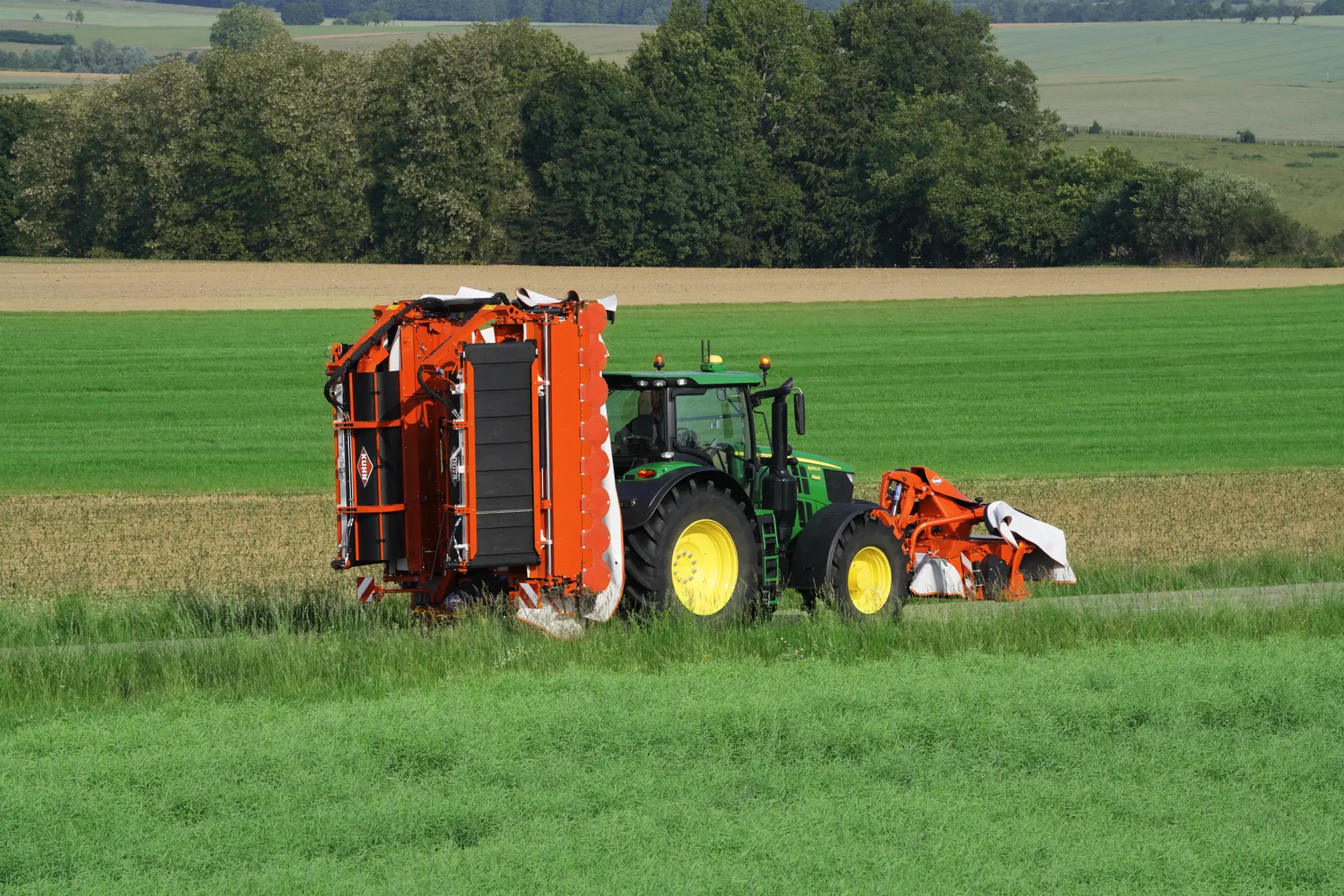 John Deere Traktor mit Kuhn Feldmaschinen auf einer Straße