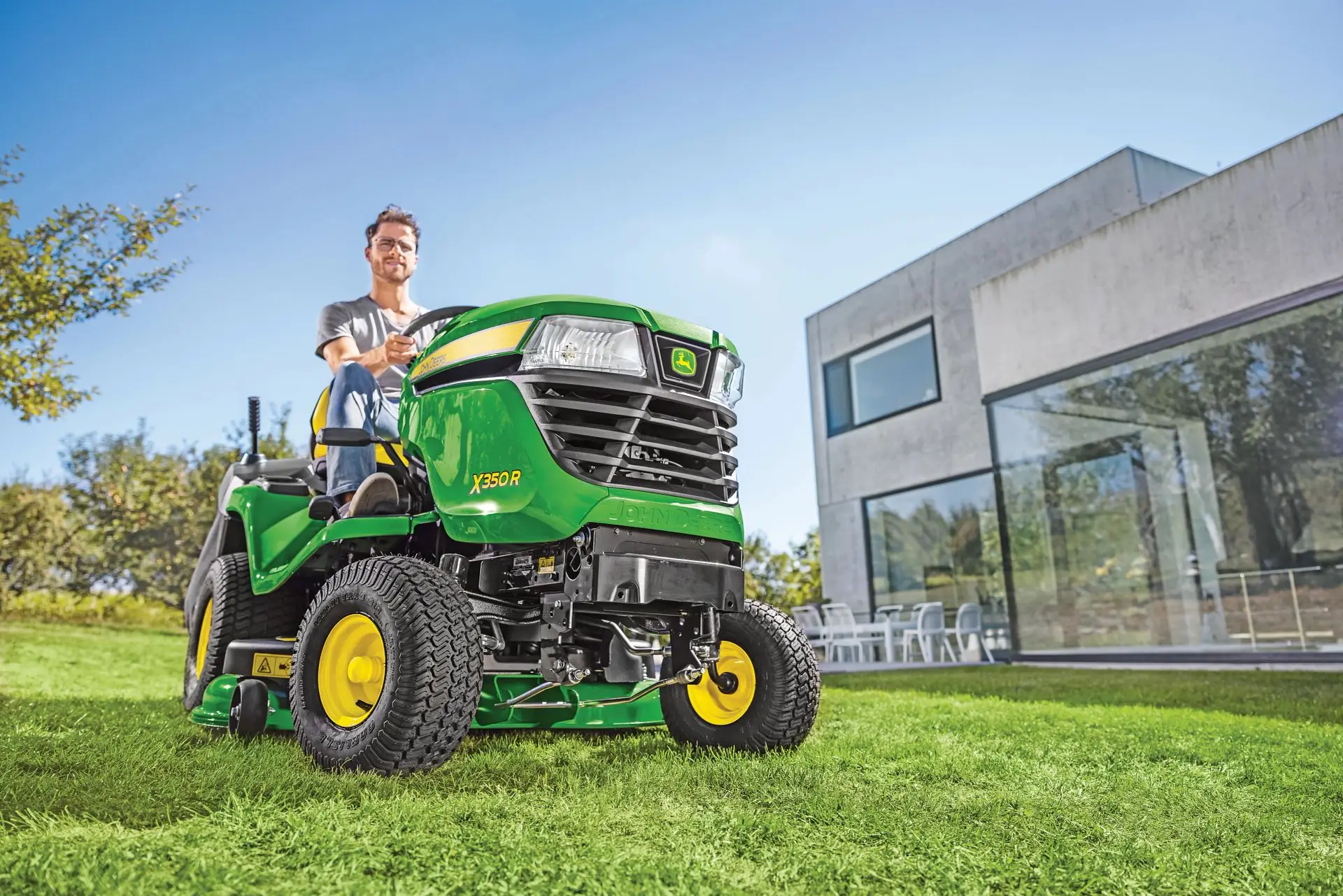Mann sitzt auf John Deere Kompakttraktor auf der Wiese