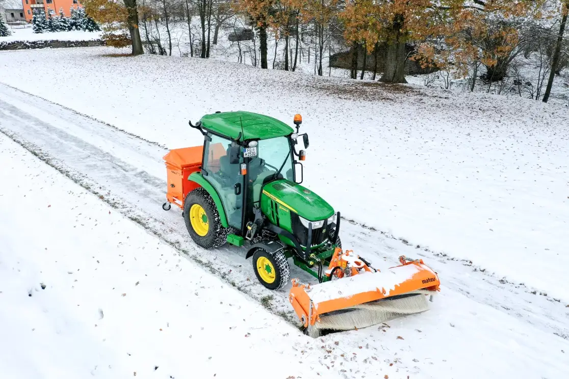 John Deere Kompakttraktor mit Schneepflug auf einer eingeschneiten Straße